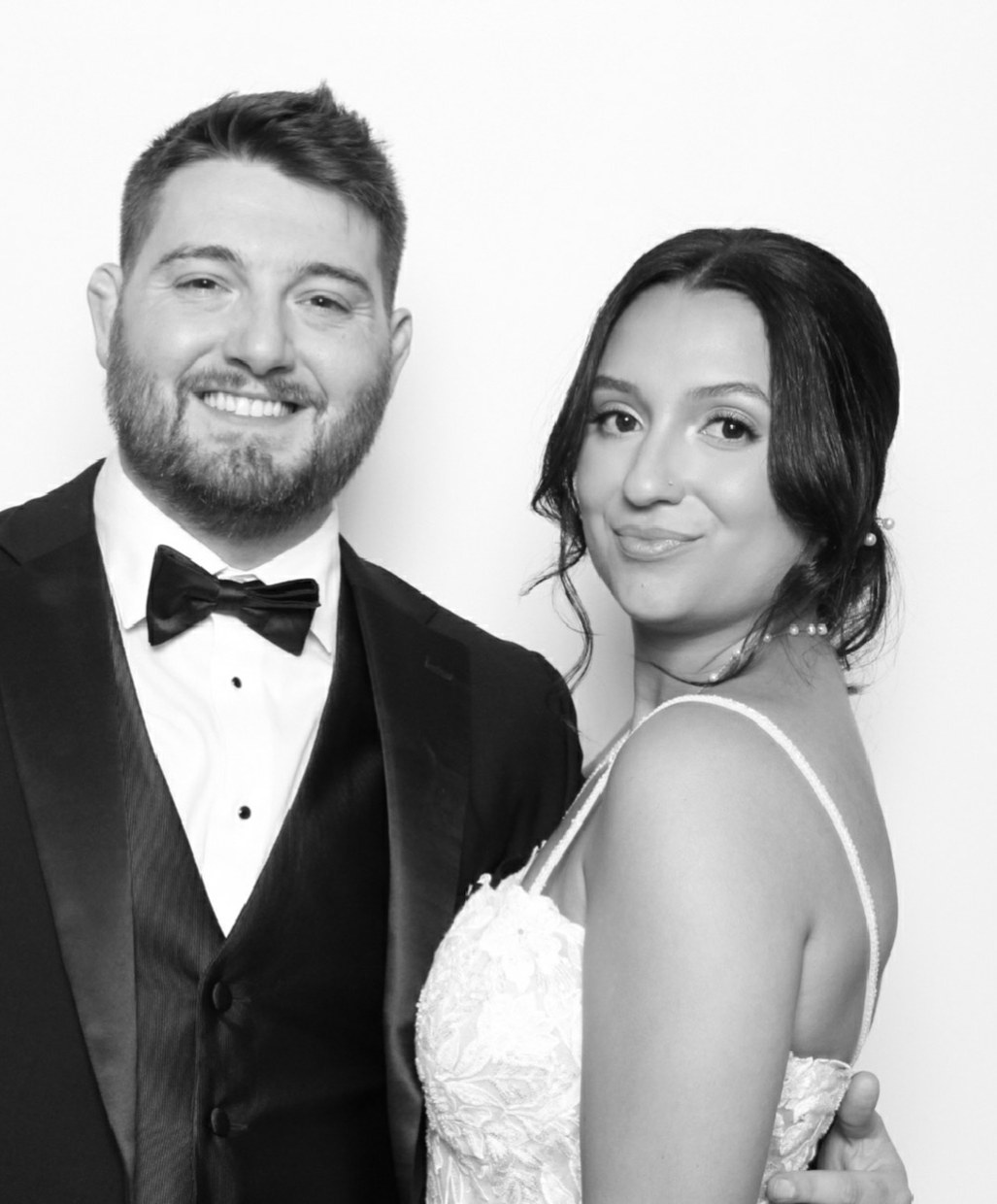 A groom in a black tuxedo and his bride photographed in black and white at the booth